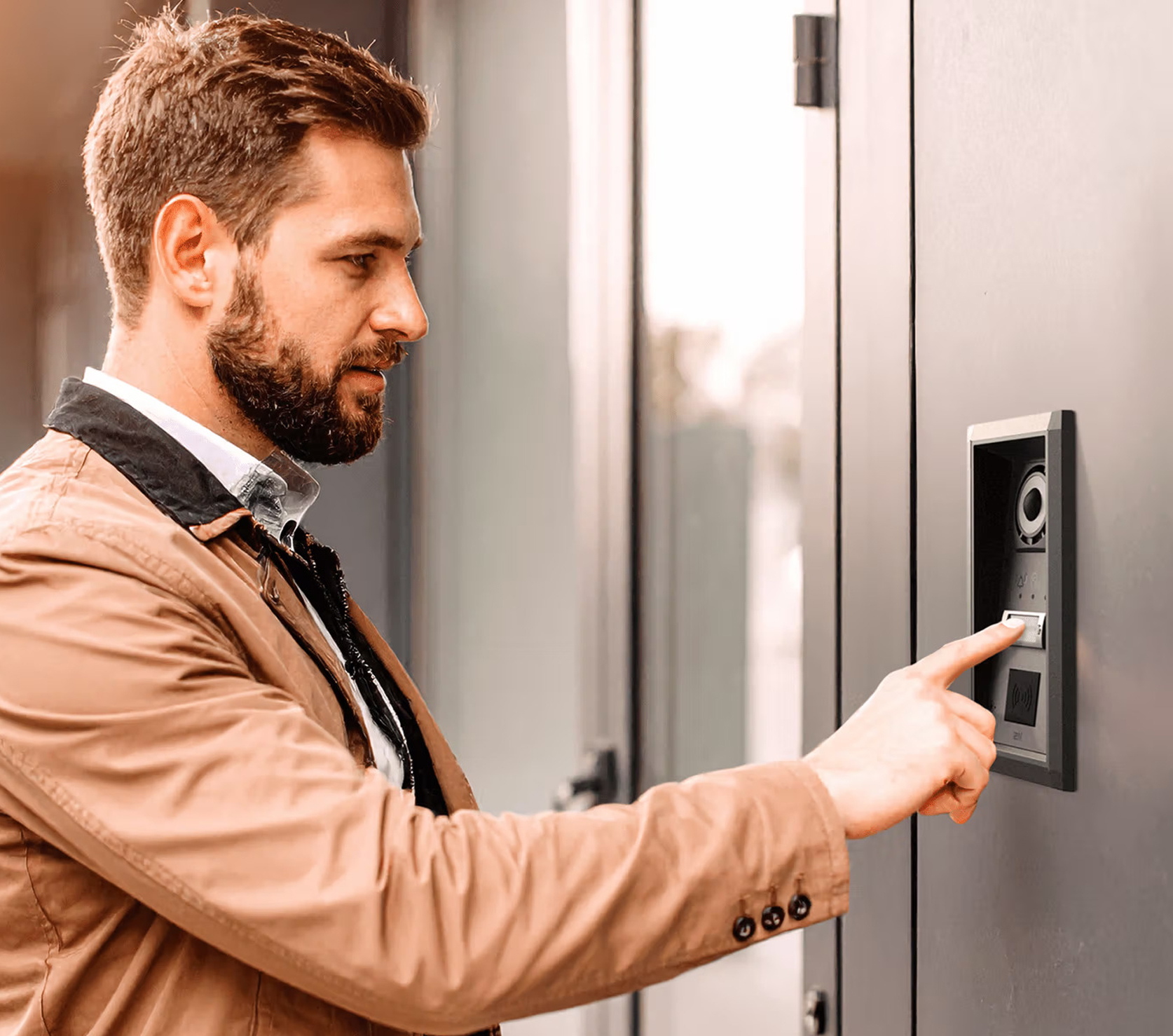 Man pressing a button on a door entry panel beside a grey front door