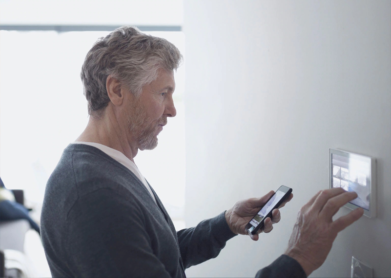Man adjusting a wall touchscreen while holding his phone