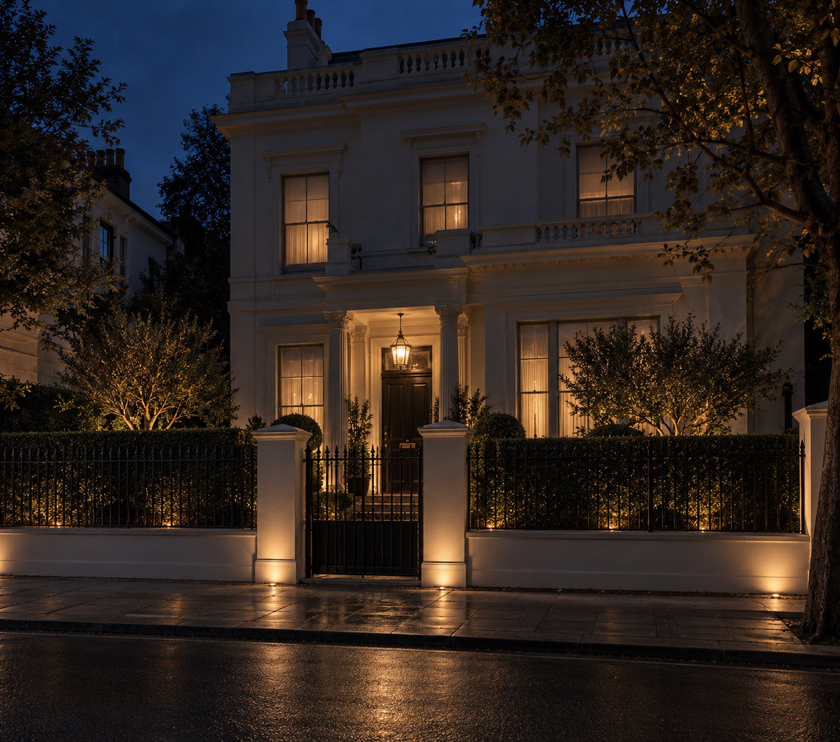 London villa at night behind its gate piers, the garden and facade softly lit