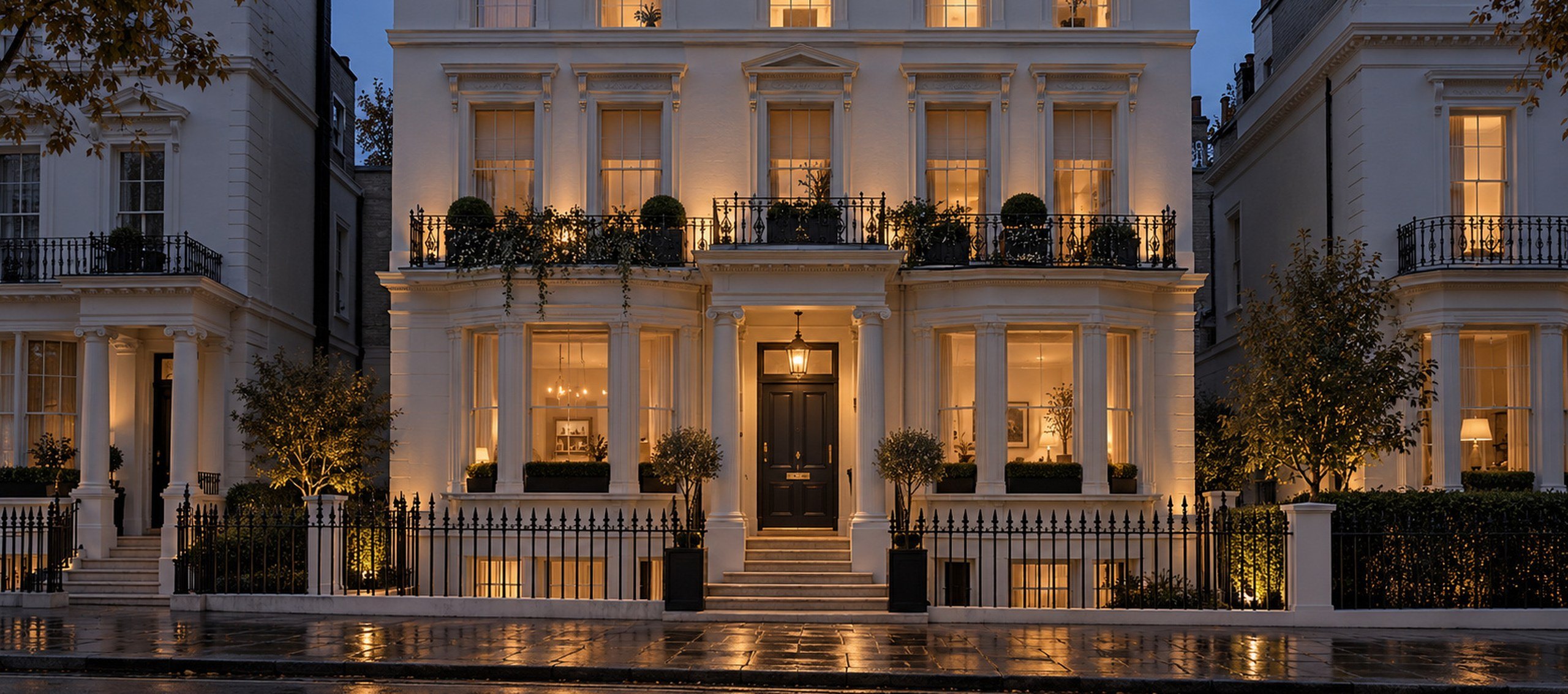 Terrace of white stucco London townhouses at blue hour, one house warmly lit