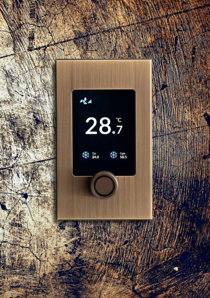 Thermostat on a bronze plate with a control knob, showing 28.7 degrees on a timber wall
